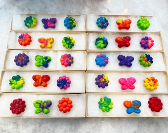 May include: A set of 10 colorful wax crayons shaped like butterflies and flowers. The crayons are arranged in rows in small boxes.
