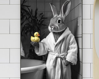 Op de afbeelding: Zwart-wit ingelijste kunstprint van een konijn in een witte badjas met een gele badeend in een badkamer. Het konijn staat bij een bad en een spiegel.