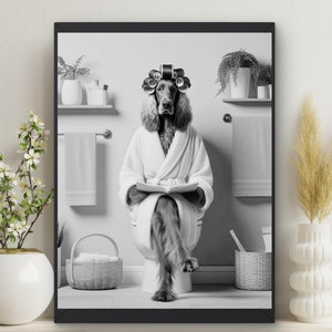 以下が含まれることがあります： バスローブとカーラーをつけた犬がトイレに座って本を読んでいる白黒写真です。