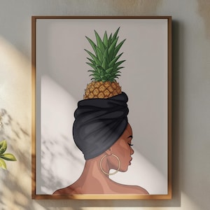 May include: A framed art print featuring a woman with a black head wrap and gold hoop earrings, topped with a pineapple. The artwork is displayed on a wooden table with a white vase of flowers, a small pitcher, and a cup of coffee.