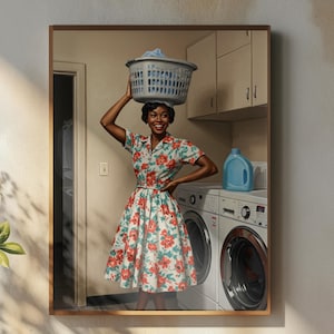 May include: A framed print depicts a woman in a floral dress balancing a laundry basket on her head. The scene includes a washing machine, detergent, and a doorway. The print is displayed on a wall above a wooden table with a vase, a teapot, and a cup of coffee.
