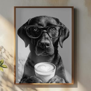 May include: Monochrome framed print featuring a Labrador wearing spectacles and holding a coffee cup with heart-shaped latte art. The print hangs above a wooden table with a coffee cup and decorative items.