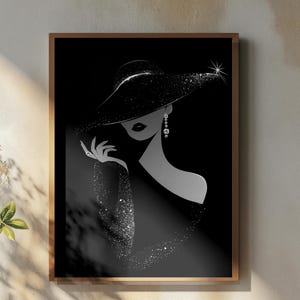 May include: A framed black and white art print of a woman wearing a wide-brimmed hat and sparkling jewelry. The artwork is displayed on a wall above a wooden table with a vase of flowers, a teapot, and a cup of coffee.