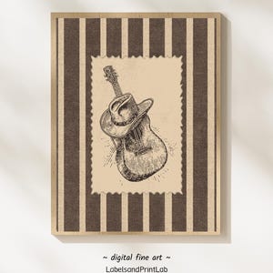 Puede incluir: Impresión digital enmarcada que presenta una ilustración en blanco y negro de una guitarra acústica con un sombrero de vaquero. La obra de arte está sobre un fondo a rayas con un borde beige.