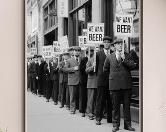 May include: Monochrome framed print depicting a historical scene. Men in suits and caps stand in a line, holding signs with the words "WE WANT BEER". The print is on a white shelf with decorative items.