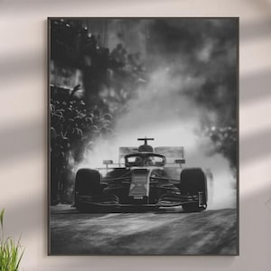 May include: Black and white framed print of a Formula 1 race car speeding down a track, surrounded by smoke. The image captures the car's front profile, emphasizing its aerodynamic design and speed. The background shows a crowd of spectators.