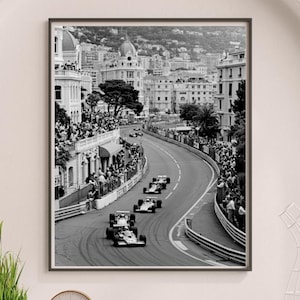 Może przedstawiać: Czarno-biała oprawiona grafika z wyścigu Formuły 1 w Monako. Obraz przedstawia samochody wyścigowe na krętym torze, otoczonym przez widzów i budynki. Fotografia oddaje energię i emocje wyścigu.