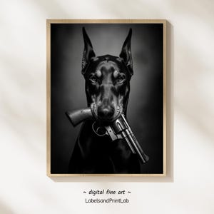 Puede incluir: Impresión digital en blanco y negro de un Doberman Pinscher sosteniendo un revólver en la boca. El perro tiene las orejas erguidas y una expresión seria. La impresión está enmarcada en un marco de madera clara. El texto "digital fine art" y "LabelsandPrintLab" está en la parte inferior.