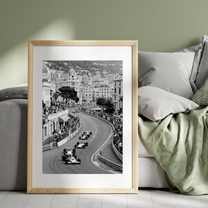 Puede incluir: Impresi&oacute;n enmarcada en blanco y negro de una carrera de F&oacute;rmula 1 en M&oacute;naco. La imagen muestra coches de carreras en una pista sinuosa, rodeados de espectadores y edificios. La impresi&oacute;n est&aacute; en un marco de madera clara.