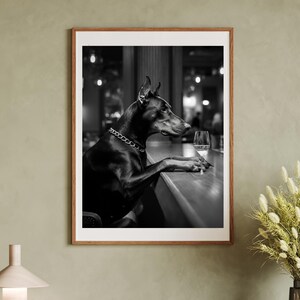 Peut inclure: Photographie en noir et blanc d'un chien Dobermann assis &agrave; un comptoir de bar avec un verre de vin. Le chien porte un collier en cha&icirc;ne dor&eacute;e.