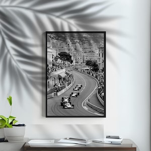Puede incluir: Impresi&oacute;n enmarcada en blanco y negro de una carrera de F&oacute;rmula 1 en M&oacute;naco. La imagen muestra coches de carreras en una pista sinuosa, con espectadores y edificios al fondo. La impresi&oacute;n est&aacute; en un marco negro.