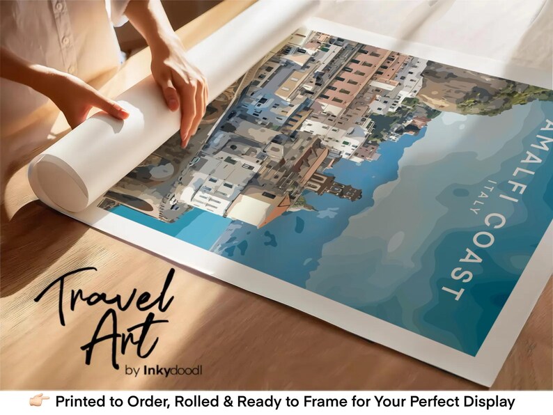 a person's hands rolling up a large poster or canvas that displays a colorful illustration of a coastal town. The poster is titled "Amalfi Coast Italy" and is described as a travel art piece. The image is printed to order, rolled, and ready to frame for your perfect display.