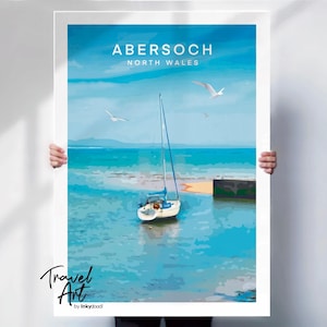 May include: Abersoch, North Wales travel art print. The poster features a sailboat on turquoise water, with seagulls in the sky. The text "Abersoch North Wales" is at the top. The artwork is signed "Travel Art by lekyddoodi".