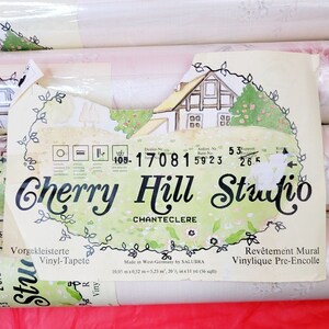 May include: A roll of wallpaper with a white background and a green, yellow, and pink floral pattern. The wallpaper is labeled "Cherry Hill Studio - Chanteclere" and has a design number of 17081. The wallpaper is made in West Germany by Salubra and is 20 inches by 11 yards.