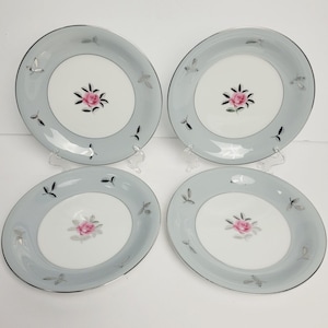 May include: Set of four grey and white ceramic dinner plates with a silver rim and a pink rose design.