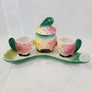 Könnte beinhalten: Ein Keramik-Servierset mit einem Kaktus-Design in Grün, Gelb und Rosa. Das Set enthält einen Milchkännchen, zwei Tassen und ein Tablett.