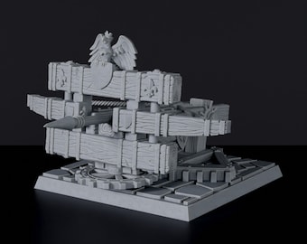 May include: A gray 3D printed model of a medieval siege weapon, a trebuchet, with a wooden frame and a large stone projectile. The trebuchet is mounted on a base with a gear mechanism. The model features a sculpted eagle with a shield on its chest.