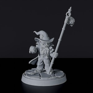 May include: A gray painted miniature figurine of a dwarf wizard wearing a pointed hat and holding a staff with a bomb at the top. The dwarf is holding a small orb in his left hand. The miniature is standing on a round base.