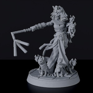 May include: A grey figurine depicting a skeletal figure with a headdress, holding a staff, and surrounded by cat-like creatures. The figure wears a draped garment and stands on a circular base.