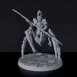 May include: A gray, detailed miniature figurine of a humanoid creature with a pointed helmet, riding a spider-like creature with multiple legs. The creature is holding a spear in its right hand. The figurine is posed in a dynamic action pose, with the spear raised above its head. The figurine is set on a circular base with a textured surface.