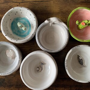 May include: Six ceramic bowls with various designs. The bowls are white with black dots and feature different animal figurines, including a fish, a seahorse, and a cactus.