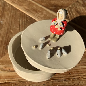 Vaso de cerâmica rústico feito à mão com uma senhora idosa alimentando pombos.