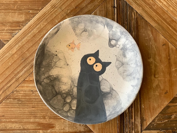 A handmade ceramic plate shaped around a black cat figure — the kind of sculptural ring dish that actually sits on a desk as art.