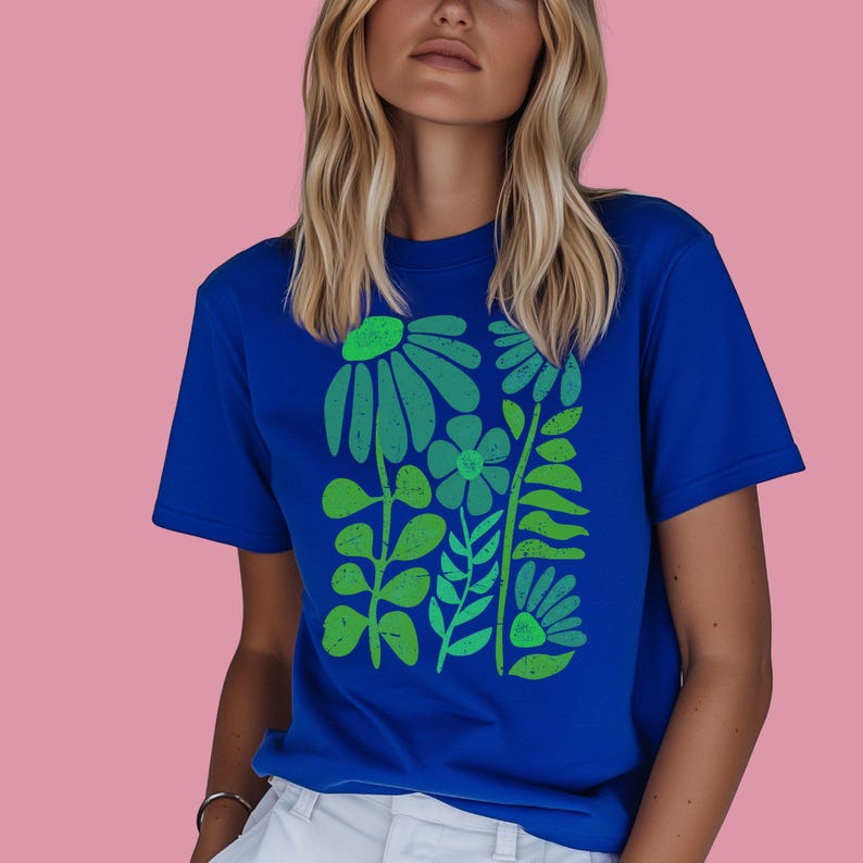 May include: A royal blue t-shirt featuring a green floral design. The graphic includes stylized flowers, leaves, and stems in varying shades of green. The shirt is a solid color with a crew neck and short sleeves.