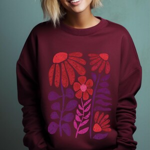 May include: A maroon sweatshirt with a graphic print of stylized red, pink, and purple flowers. The flowers are arranged in a vertical pattern and have a vintage, retro aesthetic.
