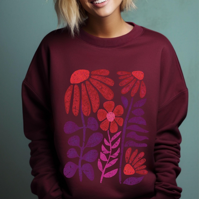 May include: A maroon sweatshirt with a graphic print of stylized red, pink, and purple flowers. The flowers are arranged in a vertical pattern and have a vintage, retro aesthetic.