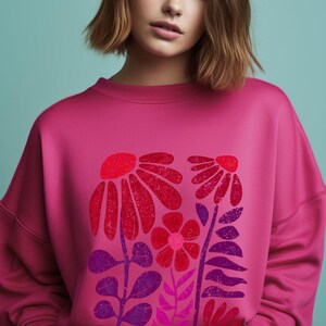 May include: A pink sweatshirt with a floral print featuring red, pink, and purple flowers and leaves. The flowers have a distressed, vintage look.
