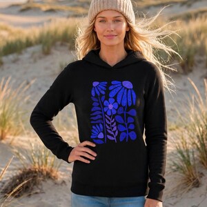 May include: A black hooded sweatshirt featuring a graphic print of stylized flowers and leaves in shades of blue and purple. The hoodie has long sleeves and a front pocket, with a textured, distressed appearance to the floral design on the chest.