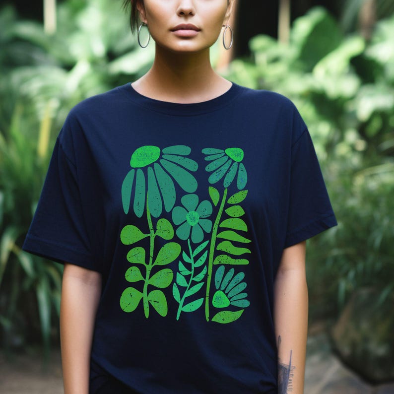 May include: Navy blue t-shirt featuring a green floral design. The graphic includes stylized flowers and leaves in various shades of green. The shirt has a classic crew neck and short sleeves.