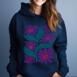 Könnte beinhalten: Ein marineblauer Hoodie mit einem grafischen Druck von stilisierten lila und pinkfarbenen Blumen mit grünen Blättern.