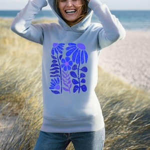 May include: A light blue hooded sweatshirt featuring a central graphic print of stylized flowers in shades of dark blue and purple. The design includes various floral shapes with a distressed texture, long sleeves, and a ribbed hem and cuffs.