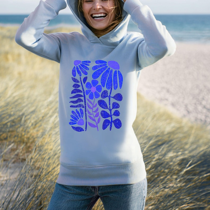 May include: A light blue hooded sweatshirt featuring a central graphic print of stylized flowers in shades of dark blue and purple. The design includes various floral shapes with a distressed texture, long sleeves, and a ribbed hem and cuffs.