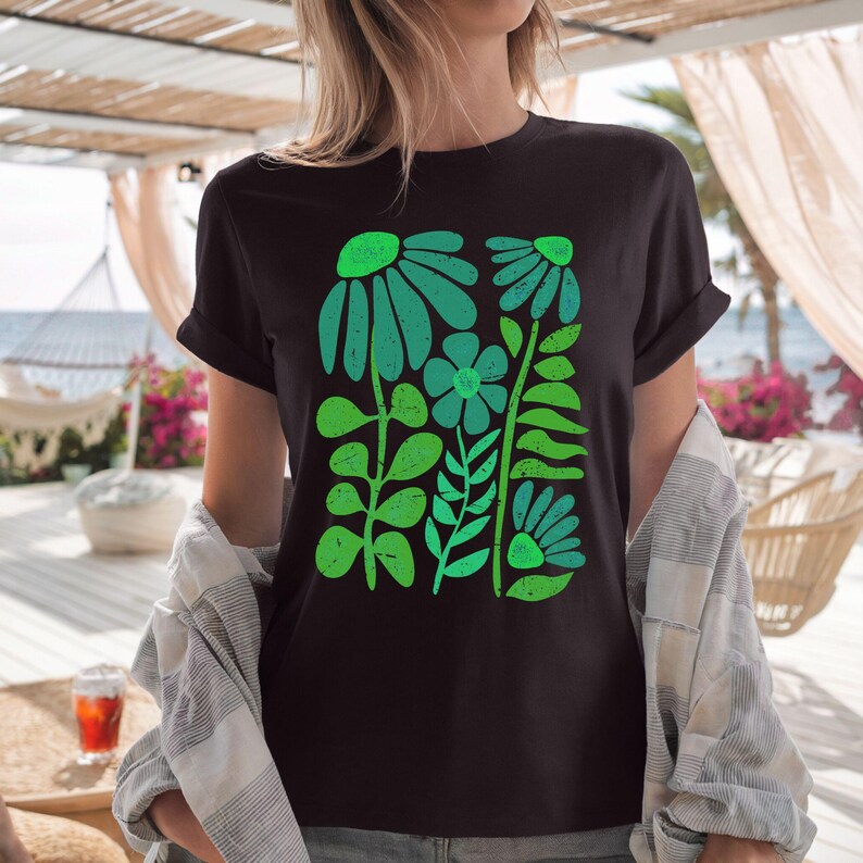 May include: Black t-shirt featuring a vibrant green floral design. The graphic includes stylized flowers and leaves in varying shades of green. The shirt has short sleeves and a crew neck.