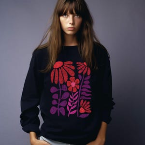 May include: A black long-sleeved sweatshirt with a colorful floral print. The flowers are red, pink, and purple and have a retro style.