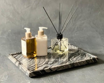 May include: A black marble tray with a white and gray swirl pattern holds three bottles. Two bottles are white with pumps and one bottle is clear with a brown liquid and black reeds.
