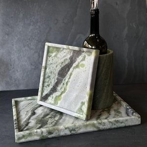 May include: A green marble wine chiller with a bottle and a square coaster, resting on a rectangular tray. The marble has a natural pattern of green, white, and grey. The wine bottle has a silver wine stopper.