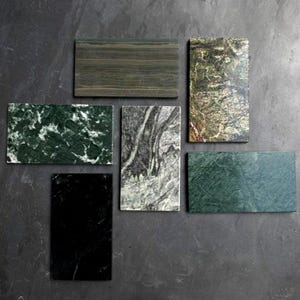 May include: Six rectangular stone tiles arranged in a cluster. The collection includes a dark brown striped tile, a mottled forest green tile, a solid black tile, a grey and white veined tile, a textured olive green tile, and a solid dark green tile.