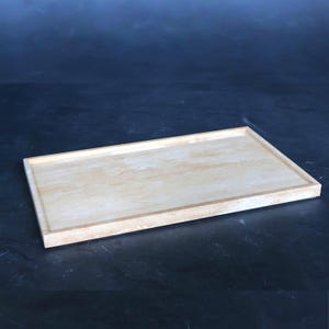 Puede incluir: Una bandeja rectangular de color claro con un borde elevado. La bandeja tiene un aspecto de piedra natural con sutiles variaciones de color, que van del beige al marrón claro. El diseño es simple y minimalista.