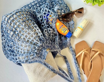 May include: A blue and white crochet tote bag with a tan towel, sunglasses, sunscreen, and a bottle of sunblock inside.