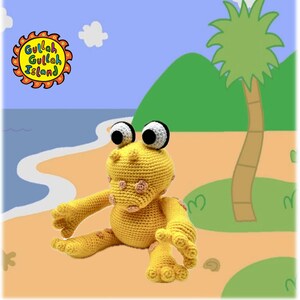 Puede incluir: Una rana de crochet amarilla con lunares rosas sentada en una playa con una palmera y agua azul. El texto "Gullah Gullah Island" está en forma de sol en la esquina superior izquierda.