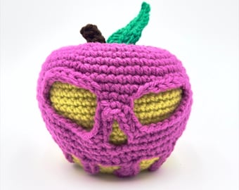 May include: A crocheted pink apple with a yellow skull face. The apple has a green stem and leaf.