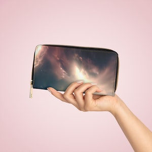 Peut inclure: Un portefeuille noir à fermeture éclair avec un imprimé galaxie coloré. Le portefeuille est tenu par une main.