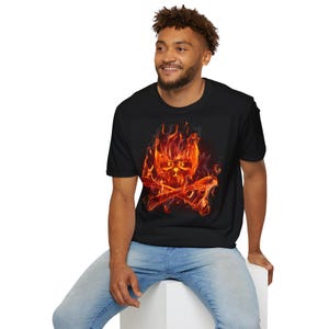 Könnte beinhalten: Schwarzes T-Shirt mit einem feurigen Totenkopf- und gekreuzten Knochen-Motiv. Der Schädel und die Knochen sind in orangefarbenen und roten Flammen dargestellt. Das Design ist auf dem T-Shirt zentriert und erzeugt einen auffälligen visuellen Effekt.