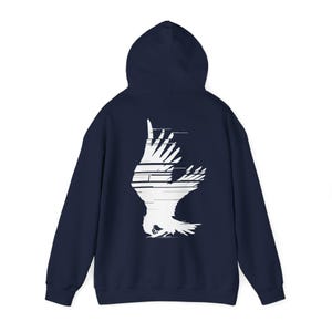 Könnte beinhalten: Ein marineblauer Kapuzenpullover mit einer weißen Grafik eines Vogels mit ausgebreiteten Flügeln. Der Vogel ist mit einem Glitch-Effekt stilisiert.