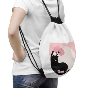 May include: White drawstring bag with a black cat sitting under a pink cherry blossom tree. The cat is silhouetted against a white background.