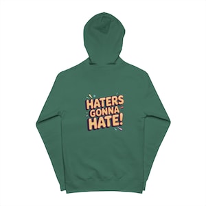 May include: A green hooded sweatshirt with the phrase "HATERS GONNA HATE!" in colorful, stylized text on the back. The hoodie has a drawstring and a kangaroo pocket.